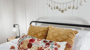 Uma cama bem arrumada com um travesseiro floral e dois travesseiros texturizados, um abajur e uma decoração de lua fixada na parede.