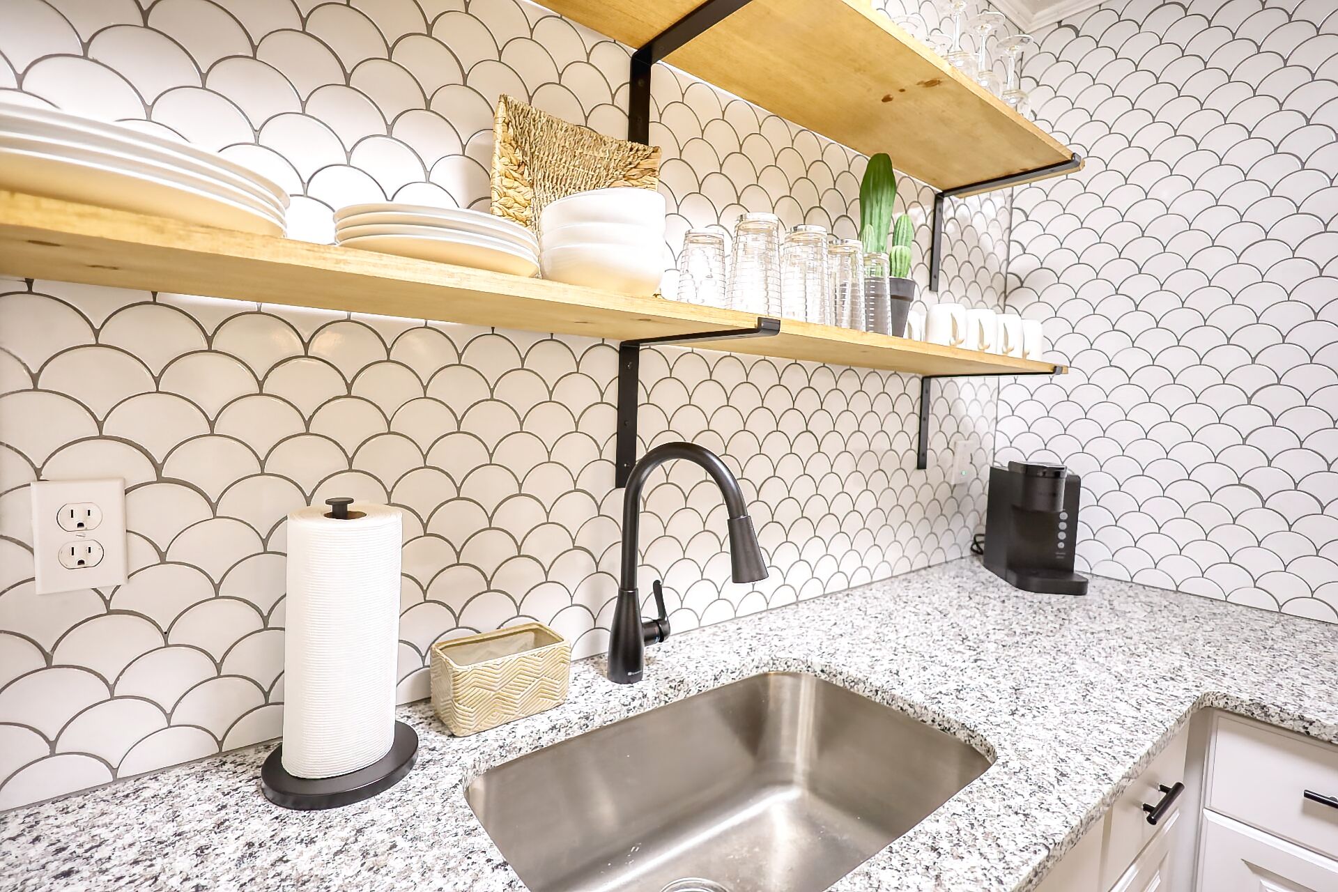 A kitchen with a granite countertop, a stainless steel sink, a black faucet, and a patterned backsplash.