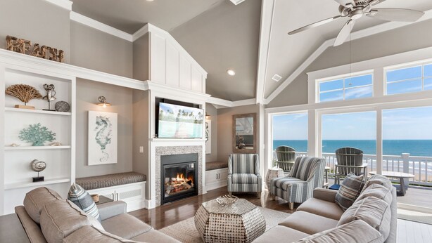 A spacious living room with a fireplace, comfortable seating, and a large window overlooking the ocean. - Coastal LunaSea: Oceanfront, Pool, Elevator OBX (Corolla)