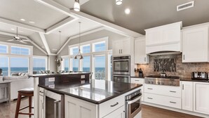 A spacious kitchen with white cabinetry, a large island, and a view of the ocean. - Coastal LunaSea: Oceanfront, Pool, Elevator OBX (Corolla)