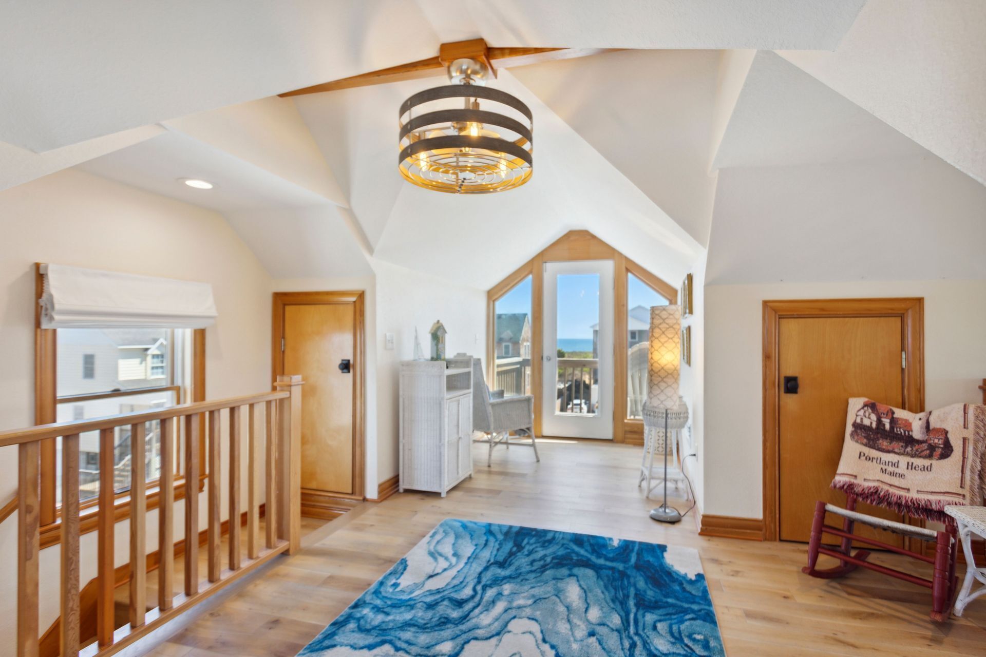 A spacious loft with a high ceiling, a wooden staircase, a large bay window, and a view of the ocean.