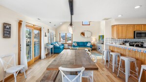 A spacious kitchen with wooden cabinets, a large island, and a dining area with white chairs. - Cedar Sandcastle*semi-oceanfront*Hot Tub*Foosball (Nags Head)