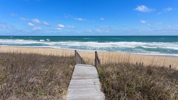 A wooden boardwalk leading to a beach with waves crashing onto the shore under a clear blue sky. - Cedar Sandcastle*semi-oceanfront*Hot Tub*Foosball (Nags Head)