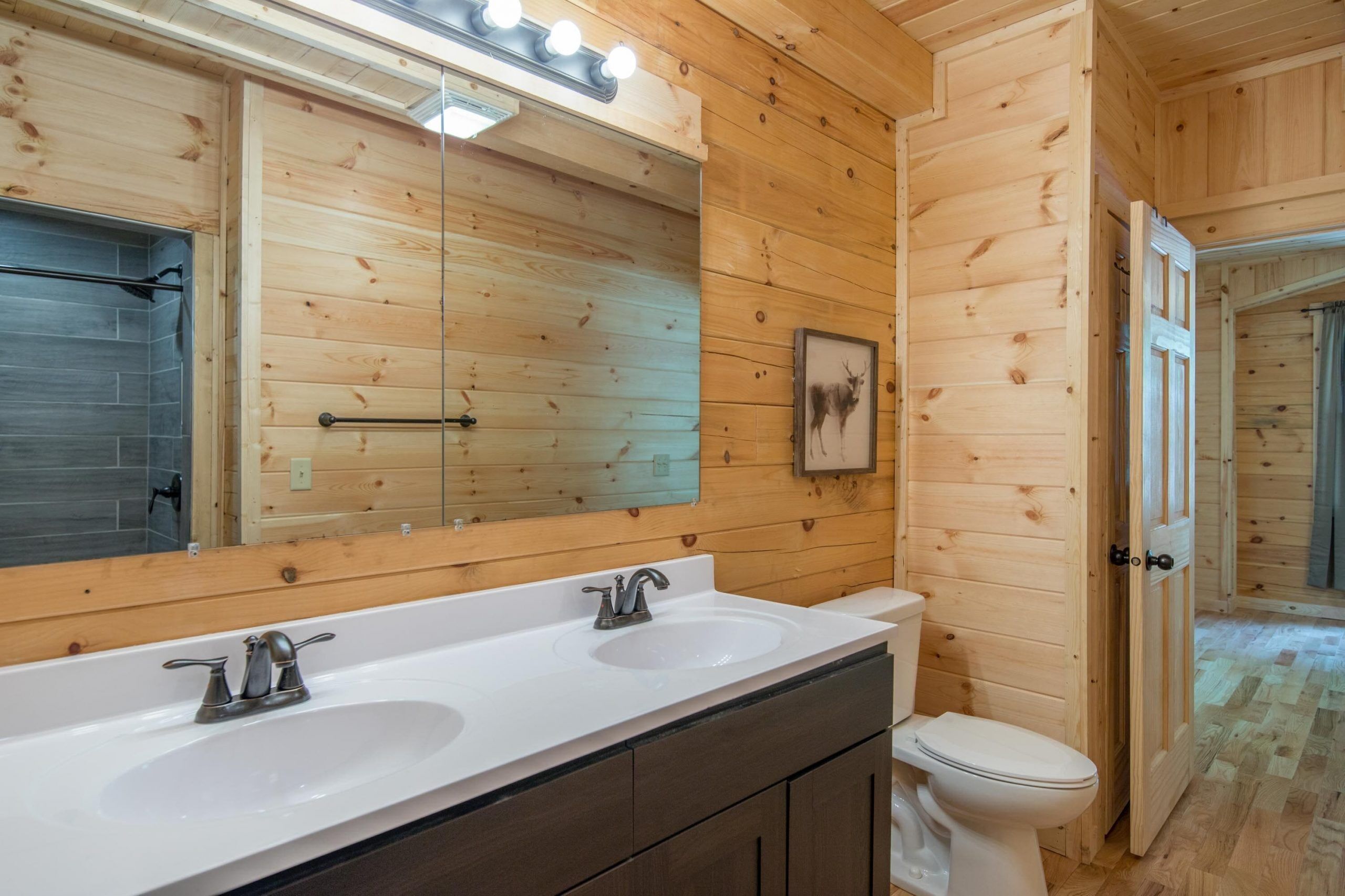 A wooden-paneled bathroom with two sinks, a mirror, and a toilet.