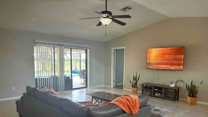Un salon spacieux avec un canapé aux couleurs foncées, une table basse et un ventilateur de plafond. Une porte-fenêtre coulissante donne accès à un espace extérieur.