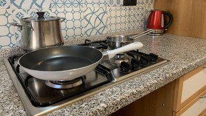 Una cocina con estufa a gas, una sartén, una olla y un hervidor.