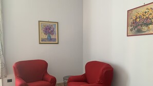 Una habitación con dos sillones rojos, una mesita redonda y dos cuadros en las paredes.