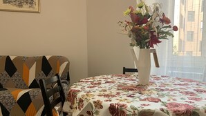 Un comedor con una mesa cubierta por un mantel floral, un sofá de estampado geométrico y un jarrón con flores.