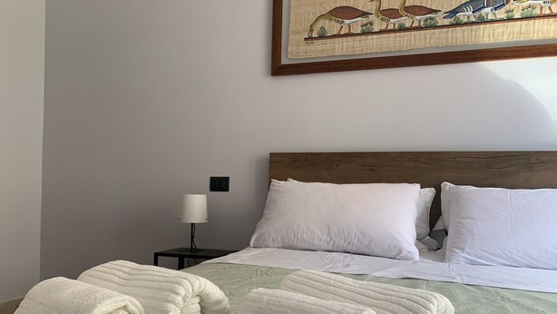 Una cama bien hecha con sábanas blancas, un cabecero de madera y un cuadro de pájaros en la pared.