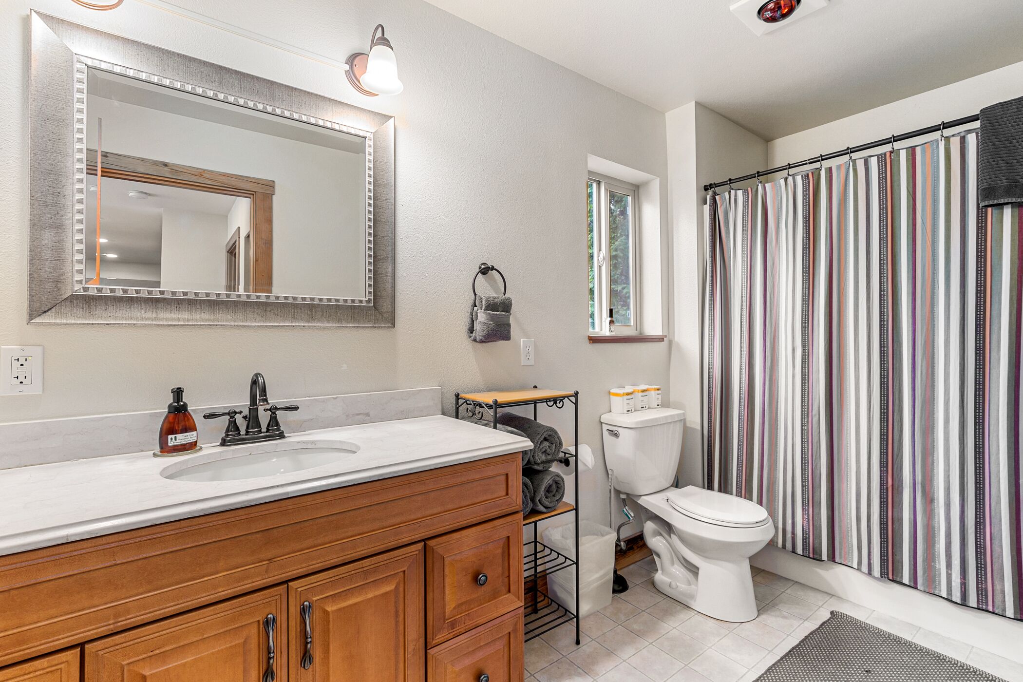 A bathroom with a white sink, wooden vanity, a large mirror, a toilet, and a striped shower curtain.