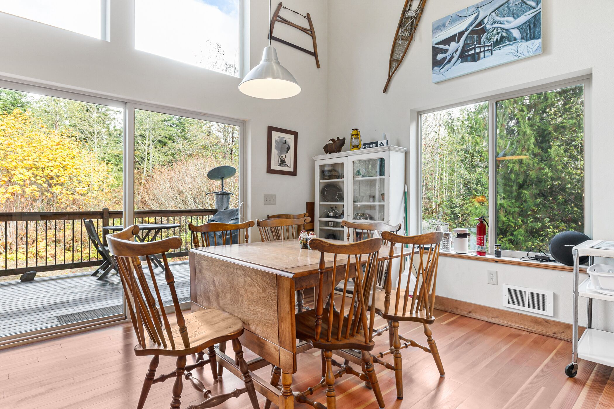 Un comedor con mesa y sillas de madera, ventanas amplias y vistas a árboles.