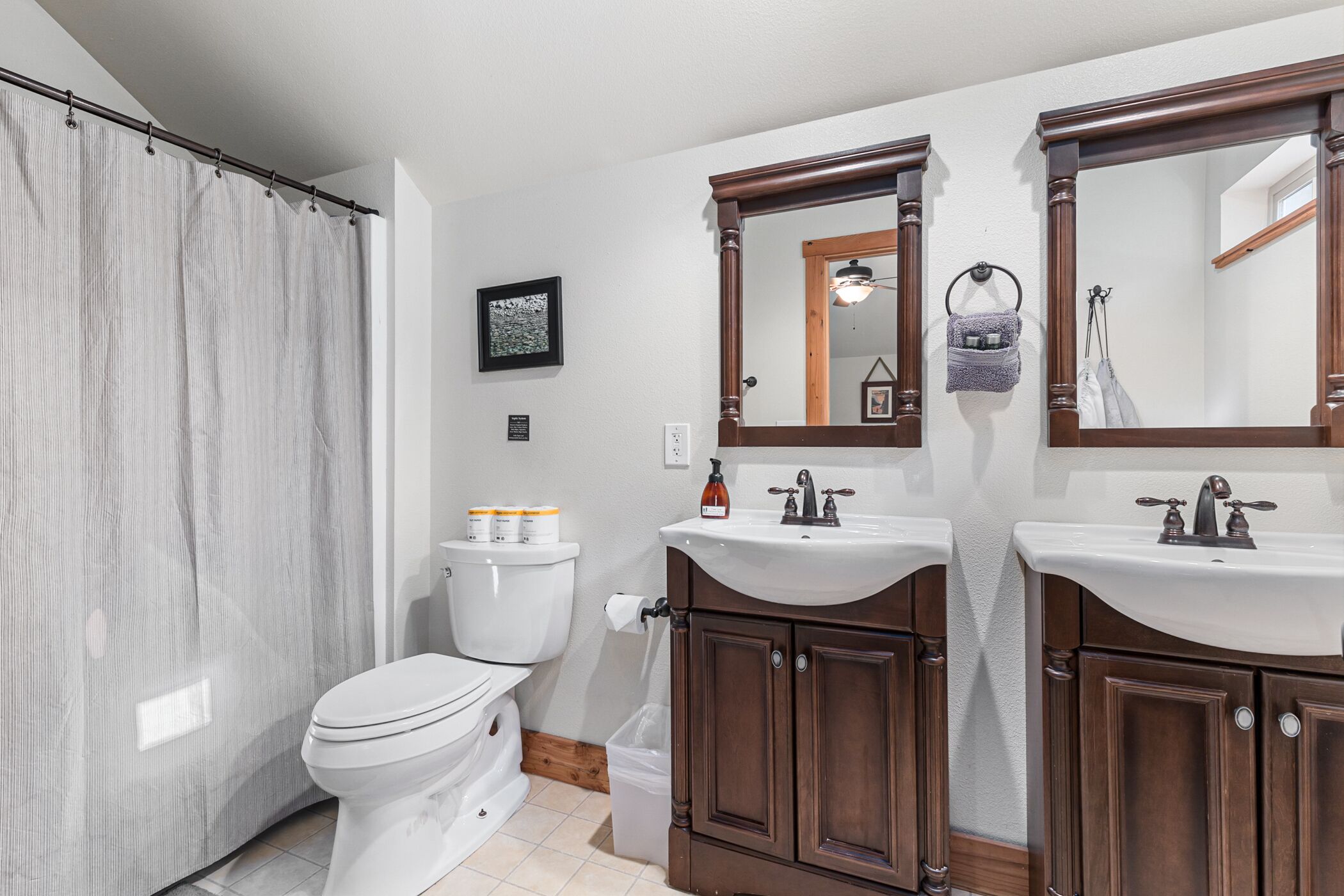 Un baño con inodoro, dos lavamanos, cortina de ducha y armarios de madera.