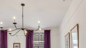 Une chambre à coucher avec un lit, un lustre, des rideaux violets, une armoire en bois et une fenêtre donnant sur des immeubles.