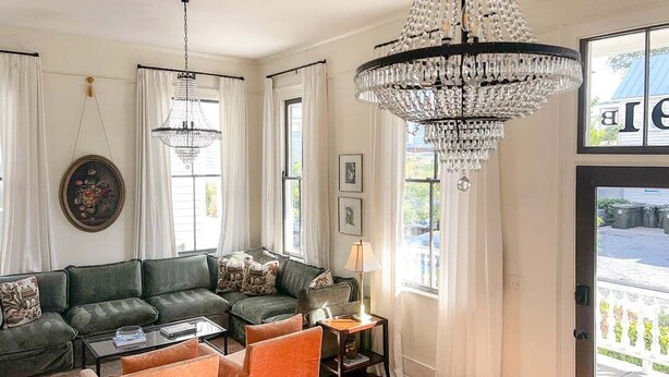 Un salon avec un canapé d’angle, des fauteuils orange, une table basse et un lustre.