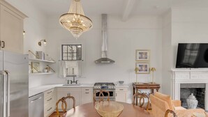 Une cuisine moderne avec des meubles blancs, un réfrigérateur en acier inoxydable, une cuisinière à gaz et un lustre.