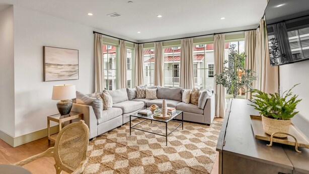 A modern living room with a sectional sofa, a coffee table, and a large window with curtains.