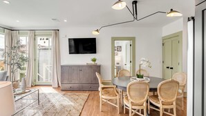 A dining area with a round table, wicker chairs, a grey cabinet, and a flat-screen TV mounted on the wall.