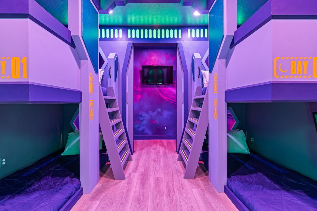 Ein modernes, mehrgeschossiges Zimmer mit Stockbetten, einer zentralen Treppe und einer neonbeleuchteten Decke.