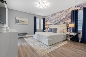 A modern bedroom with a large bed, a bedside table, a lamp, and a wall with a marble-like pattern. - Marvelous Muirfield | 10 BR, Ultra Themed Kids Rooms, Movie Theater (Kissimmee)