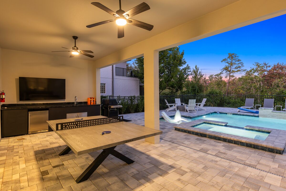 Un área exterior moderna con piscina, mesa de comedor y televisor.