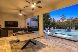 A modern outdoor living area with a pool, a dining table, and a TV.