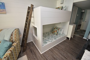 A bunk bed with a ladder, a patterned sofa, and a small cabinet.