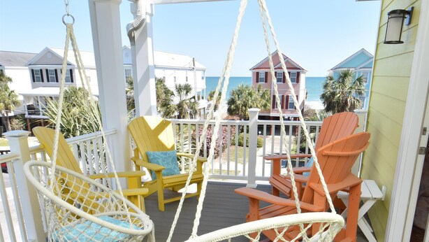 A porch with macrame chairs and a swing chair, overlooking a beach with houses in the background. - Surfside Breezes - Second Row in Surfside Beach (Surfside Beach)