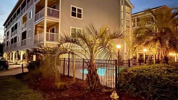 Un hotel a più piani con balconi, piscina e giardino curato.