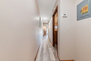 Een gang met een houten vloer, een deur aan de rechterkant en een rookverbodsbord aan de muur.
