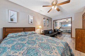A bedroom with a large bed, a wooden headboard, a ceiling fan, and a mirror reflecting the room.
