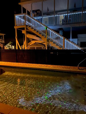 A pool with a wooden deck and a staircase leading to an upper level.