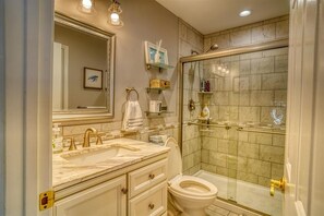 Une salle de bain dotée d’une douche à parois de verre, de toilettes, d’un lavabo avec un plan de travail en marbre et d’un grand miroir.