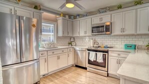 Una cocina con gabinetes blancos, electrodomésticos de acero inoxidable, un microondas y un ventilador de techo.