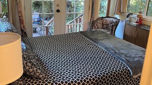 Un dormitorio con cama, mesita de noche, lámpara, control remoto y ventana con cortinas.