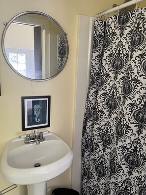 A bathroom with a white sink, a framed seahorse picture, a mirror, and a black and white patterned shower curtain.