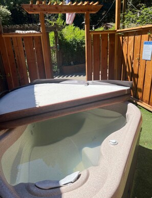 A hot tub with a wooden pergola overhead, surrounded by a wooden fence and greenery.