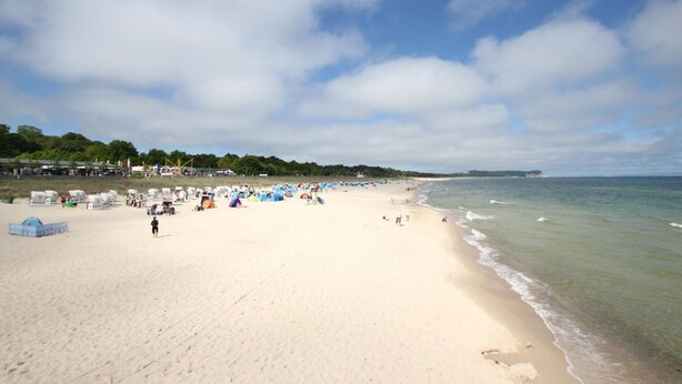 A wide sandy beach with tents and people, a clear sky, and a calm sea.
