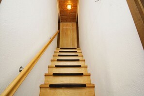 A wooden staircase with a handrail, leading to a room with a wooden ceiling and a light fixture.