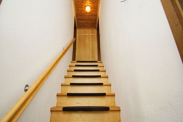A wooden staircase with a handrail, leading to a room with a wooden ceiling and a light fixture.