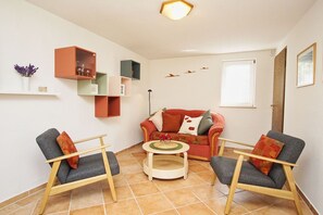 Una sala de estar acogedora con un sofá rojo, dos sillones, una mesita de centro y un estante con adornos.