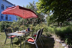 A garden patio with a table and chairs, a red umbrella, and a blue building in the background. - Ferienhaus Luki - Ostseeurlaub im Urigen Ferienhaus Luki (Göhren)