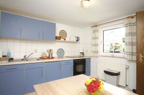 Una cocina con armarios azules, un lavamanos, una estufa y una ventana con cortinas.