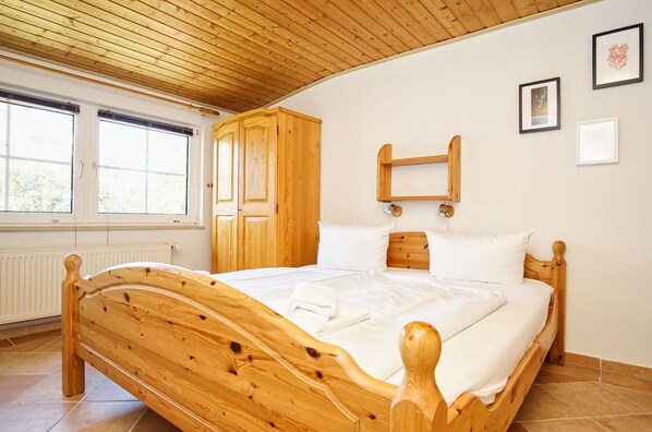 A wooden bed in a room with a sloped ceiling, a window, and a radiator.
