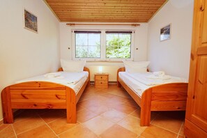 Een slaapkamer met twee houten bedden, een klein nachtkastje, een radiator en een raam met uitzicht op groen.