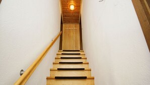 A wooden staircase with a handrail, leading to a room with a wooden ceiling and a light fixture.