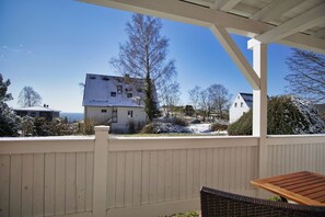 A covered patio with a wooden table and chairs, overlooking a house with a snow-covered yard and a view of the sea. - Die Ferienwohnung Nr. 01 in der Villa am Sonnenhang - Villa am Sonnenhang (Göhren)