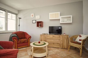 Ein Wohnzimmer mit einer Couch, einem Sessel, einem kleinen Tisch, einem Fernseher und einem Schrank.