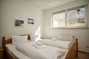 Une chambre avec deux lits, du linge de lit blanc, une fenêtre avec des stores et deux tableaux accrochés au mur.