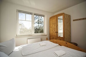 Makuuhuoneessa on sänky, puinen vaatekaappi ja ikkuna, josta on näkymä puita kohden.