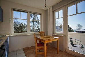 Eine Küche mit Esstisch und Stühlen, große Fenster mit Blick auf schneebedeckte Bäume und ein Balkon mit einem Stuhl.
